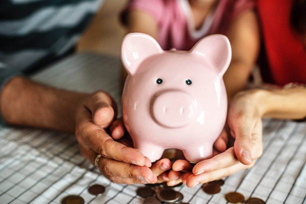 Picture of a woman holding a piggy bank. Next to the piggy bank there are coins.
